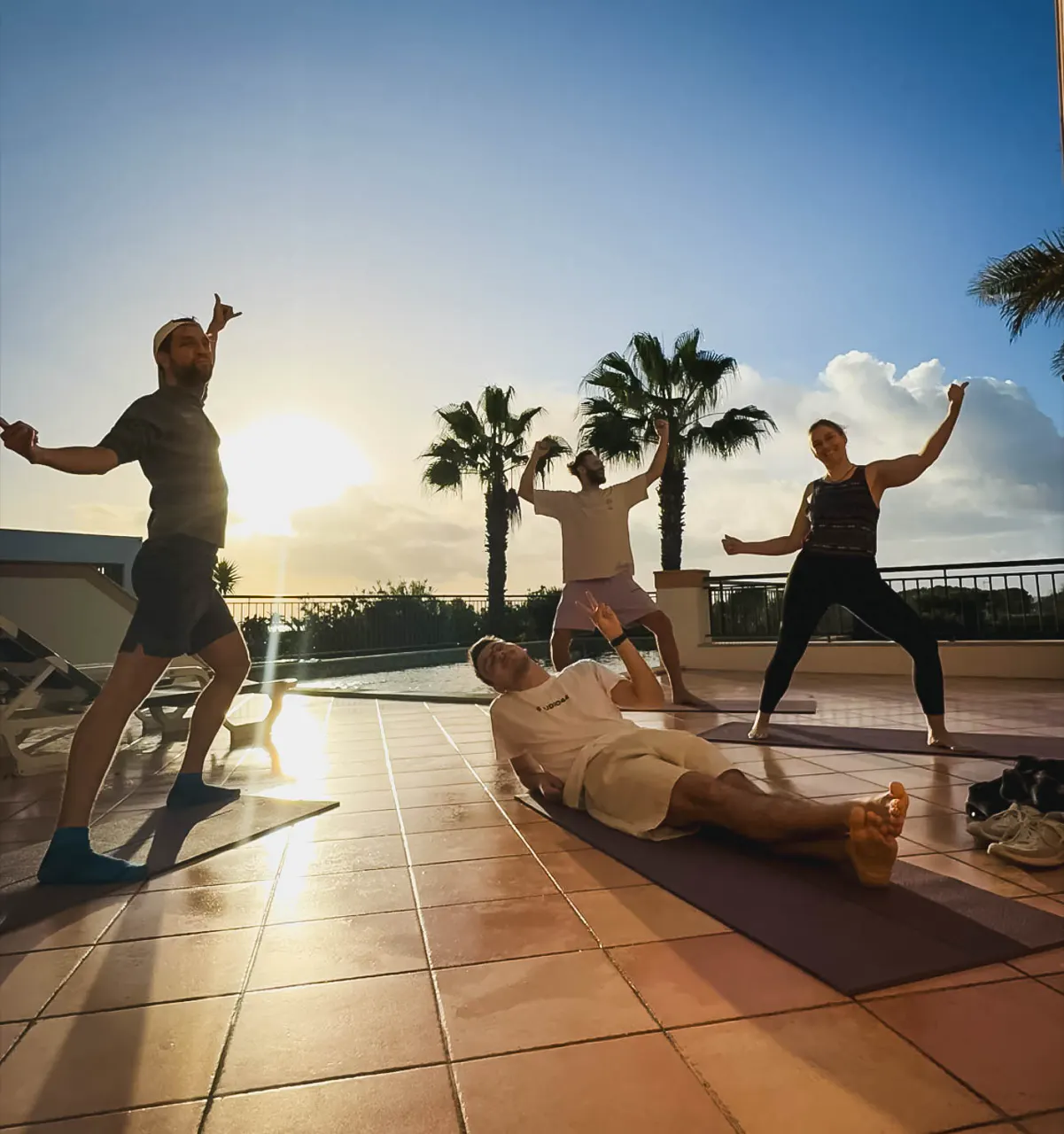 Eine Gruppe macht am frühen Morgen Yoga auf einer Terrasse, die Sonne steht tief.