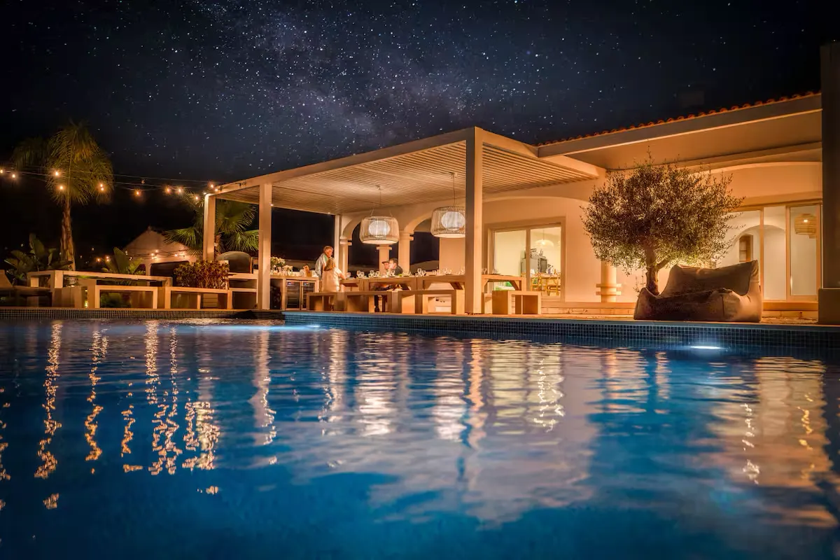 Pool bei Nacht, dahinter die beleuchtete Villa unter Sternenhimmel.